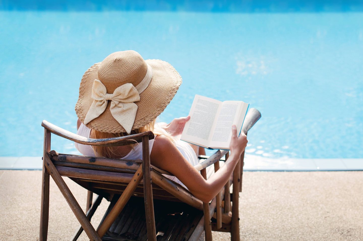 Woman reading poolside in a sun hat