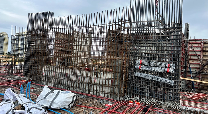 Dense rebar forming a reinforced concrete wall with conduit and materials on the slab.