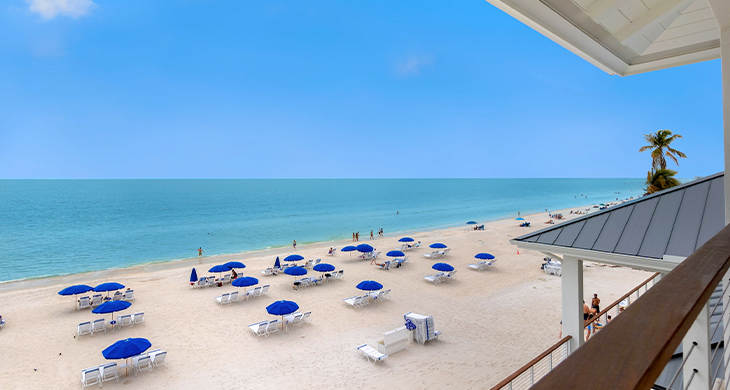 Sandy beach with blue umbrellas and white lounge chairs beside calm ocean water.