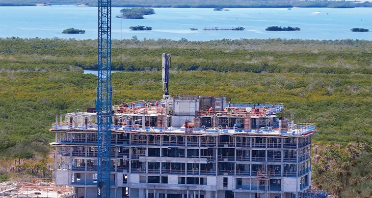 Multi-story concrete condominium under construction with crane near coastal wetlands