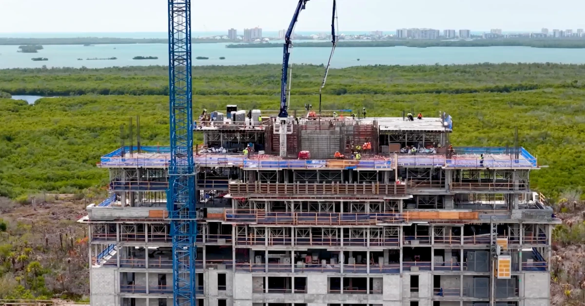 Upper floors of a high-rise under construction with workers and concrete equipment.