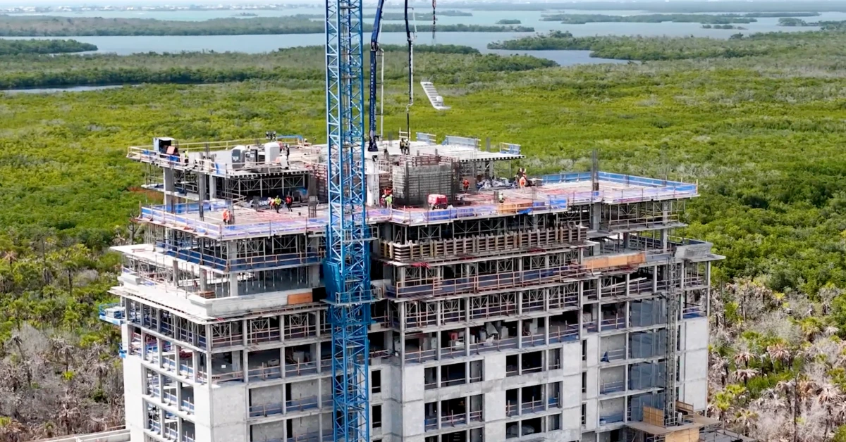 Aerial view of a high-rise under construction beside mangroves and waterways.