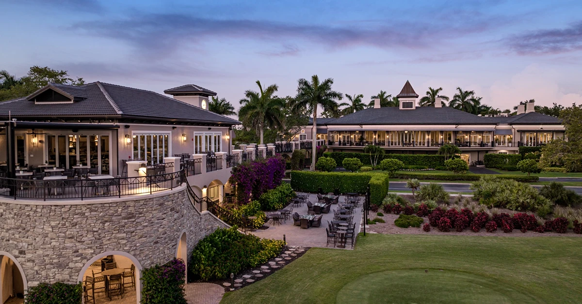 Clubhouse buildings with outdoor seating and landscaped grounds at sunset.