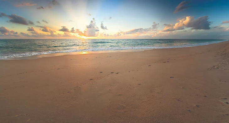 Sunrise over ocean with sandy beach and visible footprints in foreground