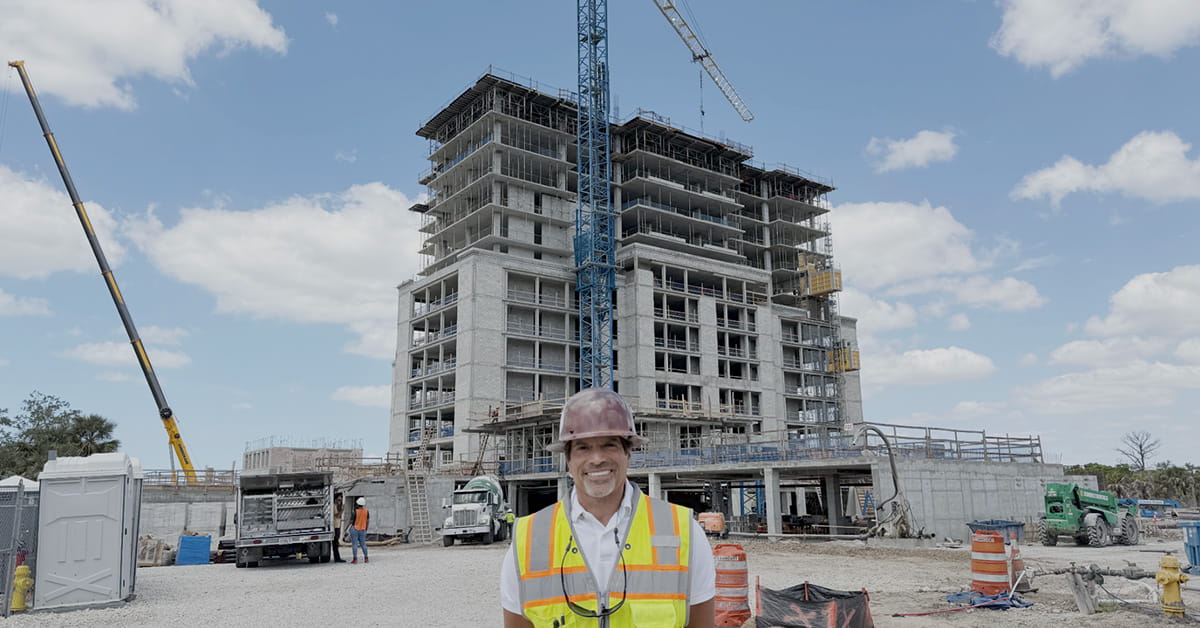 Construction worker in safety vest stands before unfinished building and crane