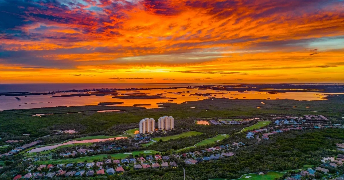 Breathtaking aerial sunset view over a luxury Florida coastal community featuring golf courses, waterways, and high-rise residences glowing in golden light.